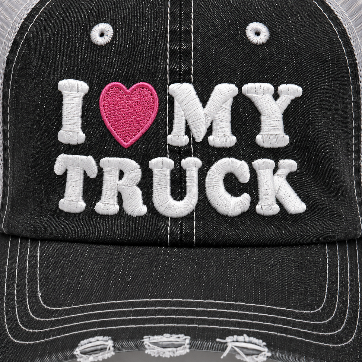 Close-up of I Love My Truck trucker hat showing white embroidered lettering, pink heart detail and distressed black fabric.