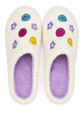 Ivory Smiley Face Fuzzy Slippers flat lay showing colorful embroidered melty smiley faces, purple daisy flowers, and rainbow accents on ivory fuzzy exterior with lavender interior
