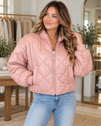 Model wearing the blush pink quilted full-zip jacket with a stand-up collar and elastic cuffs, paired with jeans
