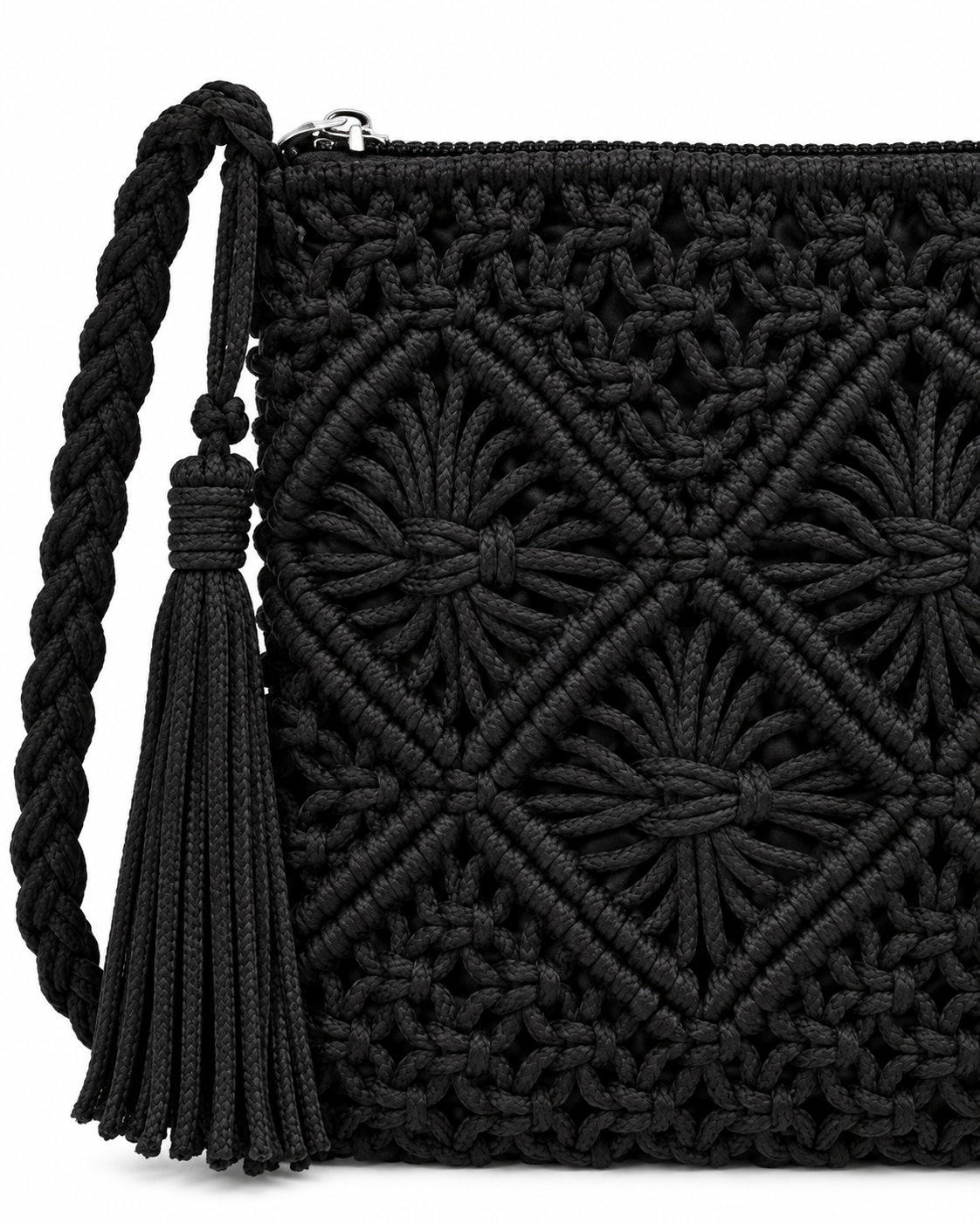 Close-up of Black Woven Bohemian Tassel Crochet Shoulder Bag showing macrame cord diamond lattice and starburst knot detail in solid black, silver zipper pull along top edge, braided cord strap knotted attachment point, and wrapped black suede tassel with cord fringe
