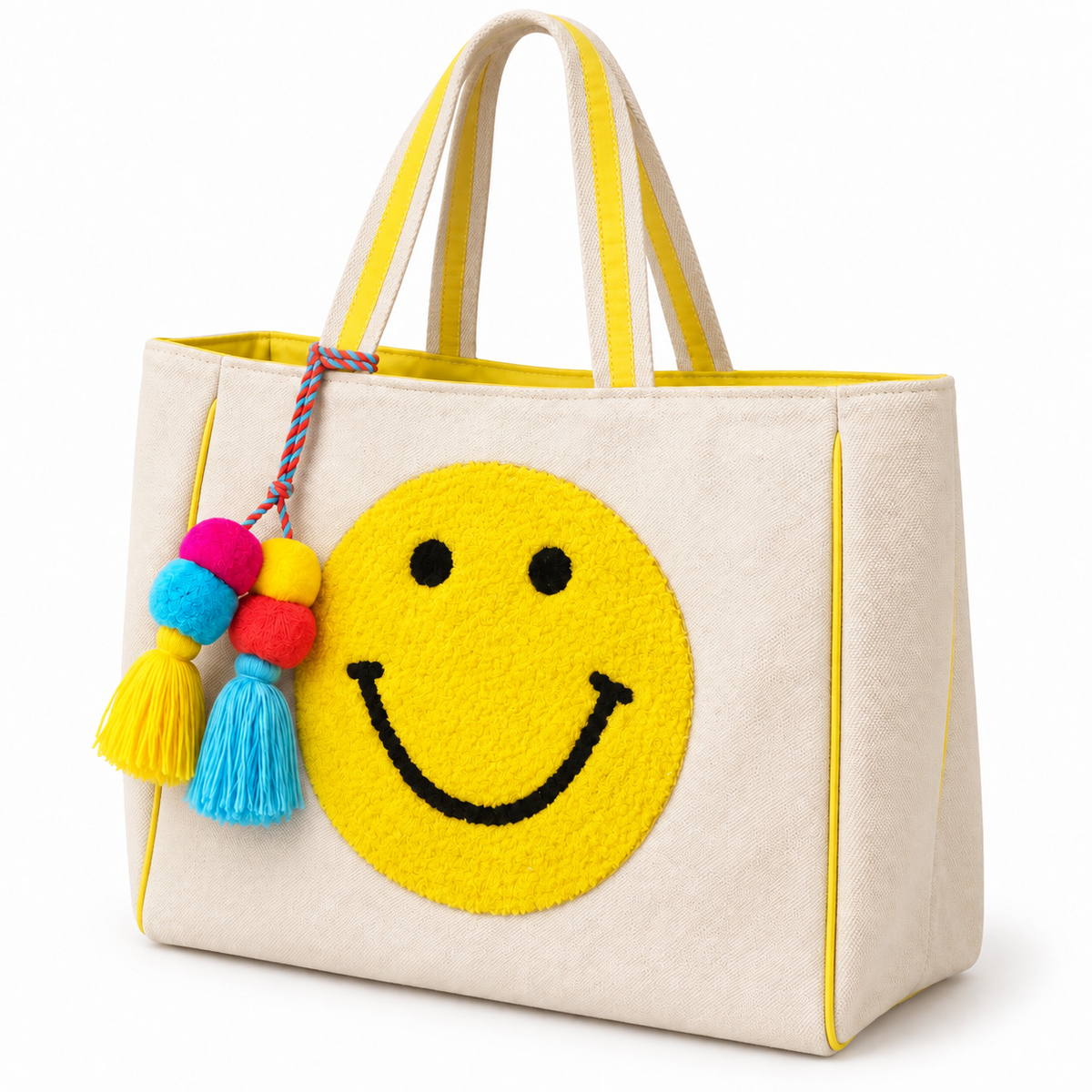 Smiley Face Tote Bag three-quarter angle view showing natural canvas body, large textured punch needle yellow smiley face, yellow striped handles, yellow trim edges, and colorful pom-pom tassel on white background
