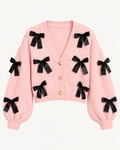 Front view of the pink cropped cardigan showing black ribbon bows, a ribbed V-neckline, three gold-tone buttons, and long sleeves
