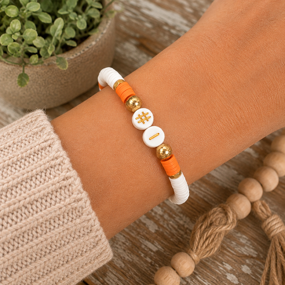 Woman wearing orange and white #1 beaded stretch bracelet on wrist with cream knit sweater and wood bead garland
