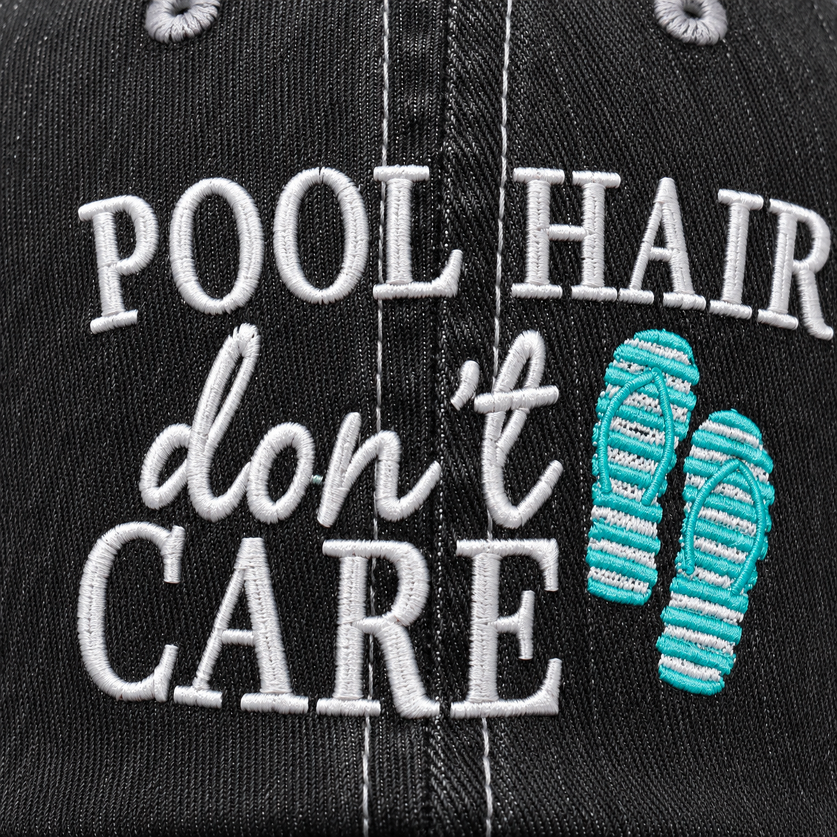 Close-up of embroidered "Pool Hair Don't Care" lettering with teal flip-flop graphic on a washed black trucker hat front panel.
