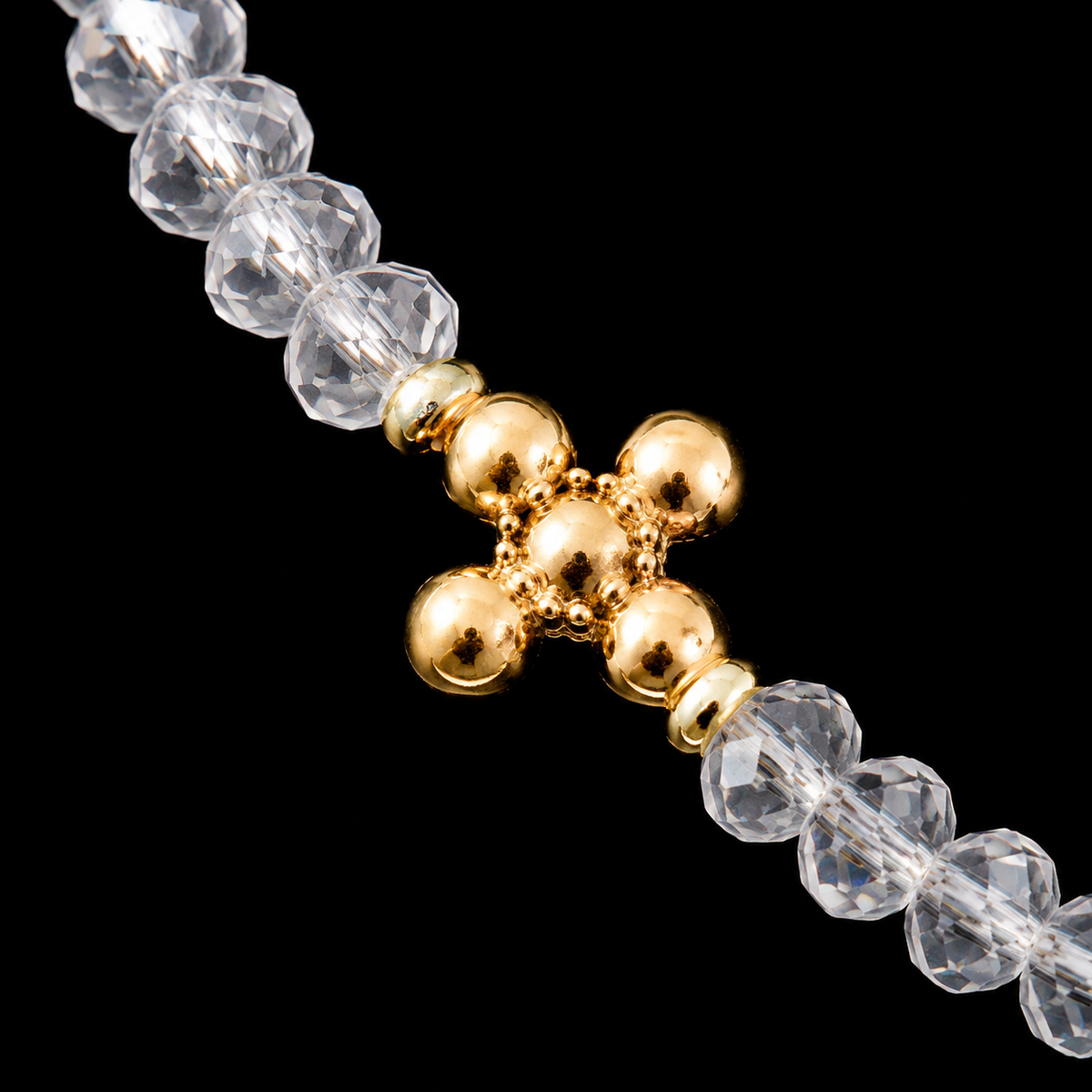 Close-up of gold cross-shaped bead accent surrounded by clear faceted rondelle beads on stretch bracelet
