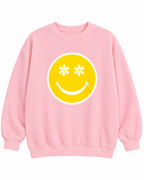 Front view of the light pink sweatshirt with a large yellow smiley face, white daisy-shaped eyes, and a white circular border
