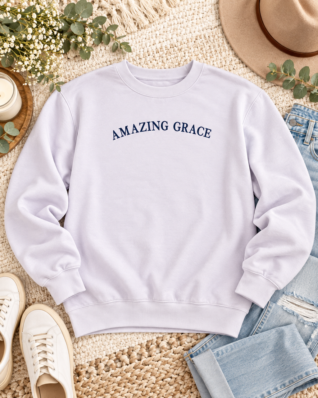 Lavender Amazing Grace sweatshirt styled flat with jeans, cream sneakers, a tan hat, and greenery
