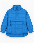 Flat lay front view of blue quilted puffer pullover jacket showing snap-flap kangaroo pocket, quarter snap placket, and curved high-low hem
