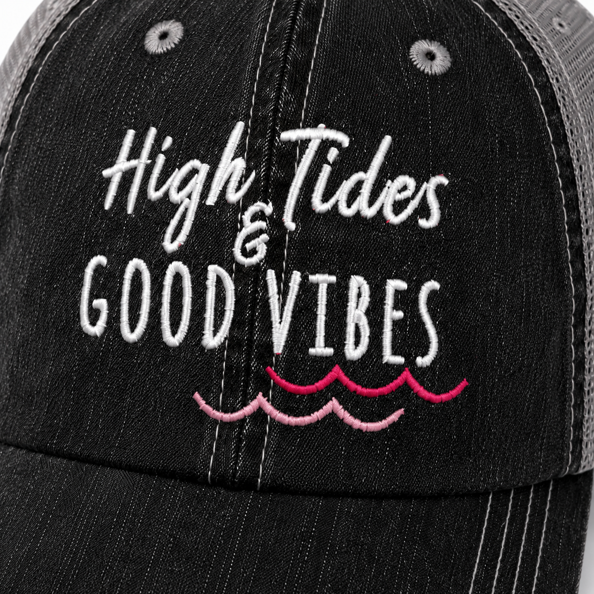Close-up of High Tides & Good Vibes embroidery on distressed black trucker hat showing white lettering and pink wave accent stitching.