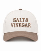 Salt & Vinegar Two-Tone Baseball Cap in Ash Mocha front view showing cream structured cotton crown with bold black embroidered Salt & Vinegar block lettering, mocha taupe bill, and mocha top button on white background
