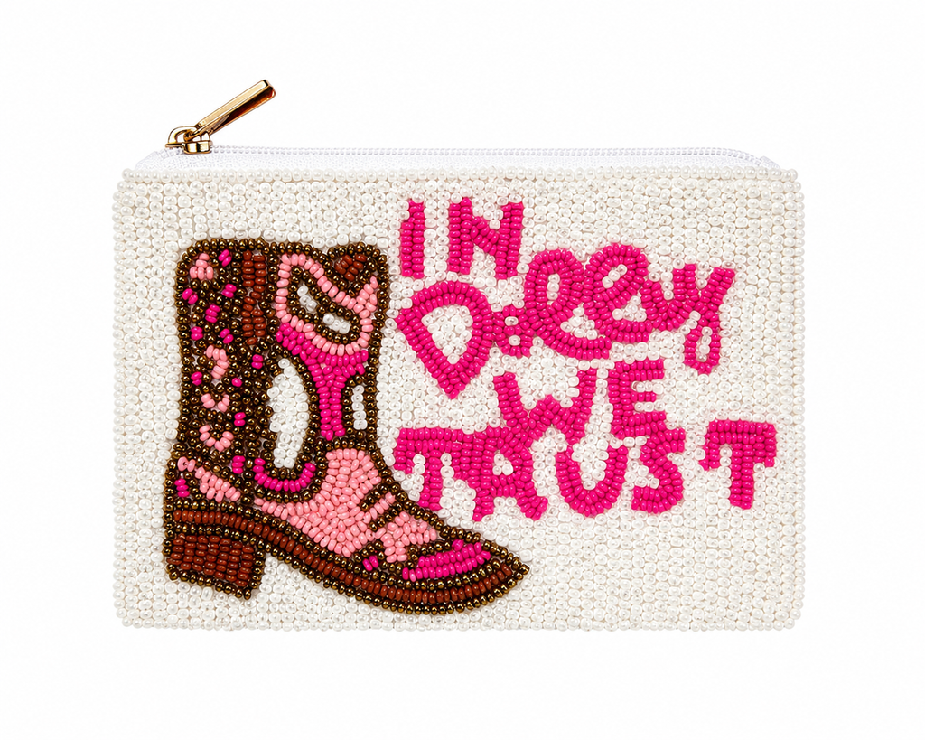 A white beaded zip pouch featuring a pink and brown beaded cowboy boot and the text 'IN DOLLY WE TRUST' in bright pink beaded lettering, with a gold zipper pull.
