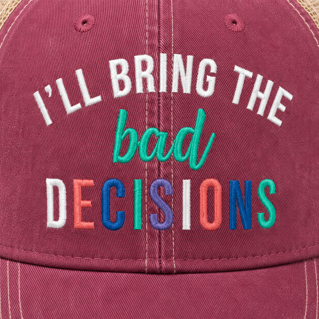A close-up of a dusty rose trucker hat featuring colorful embroidered text that reads 'I'LL BRING THE bad DECISIONS'. The cap has a textured fabric finish with visible stitching details.