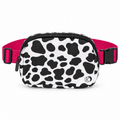 Cow Print Belt Bag front view showing rounded oval white nylon with large black cow print spots, black top zipper closure, silver Katydid K logo rivet, and hot pink webbing strap with black side-release buckle on white background
