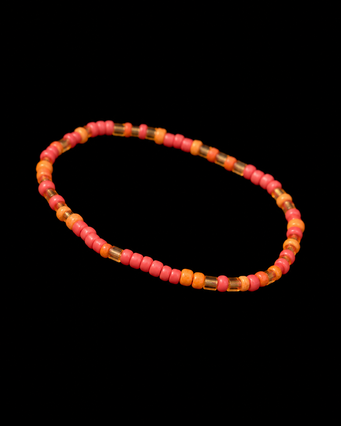 Coral and orange seed bead stretch bracelet with gold bugle beads shown at an angle on black reflective surface
