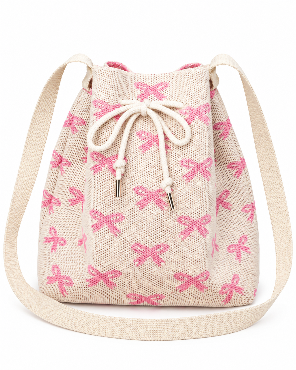 Coquette Bow Crossbody Bucket Bag front view showing cream woven knit fabric with allover pink bow pattern, cream rope drawstring closure with silver aglet tips, and wide flat cream crossbody strap with cream fabric attachment tabs on white background
