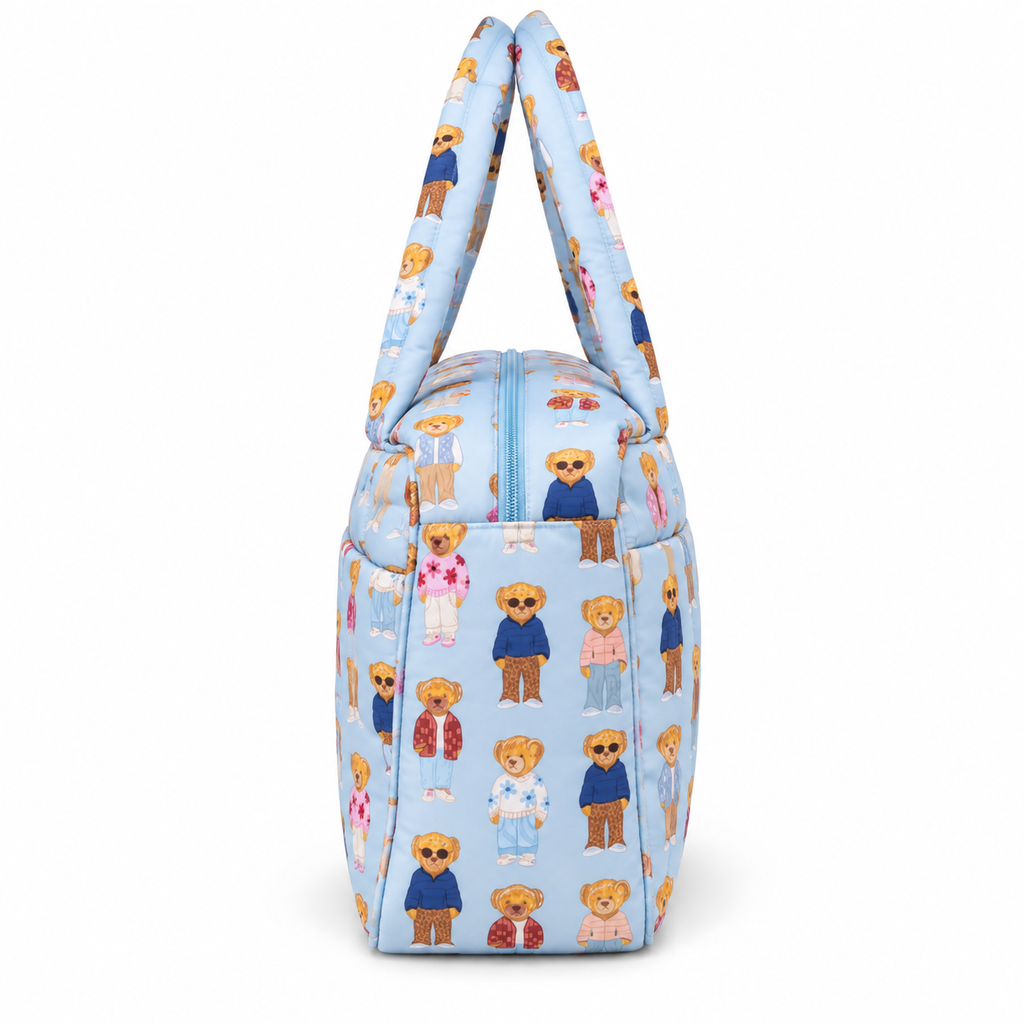 Blue Teddy Bear Weekender Bag side view showing light blue quilted nylon with allover teddy bear print, structured gusseted side panel depth, light blue top zipper curve, and dual padded print handles on white background
