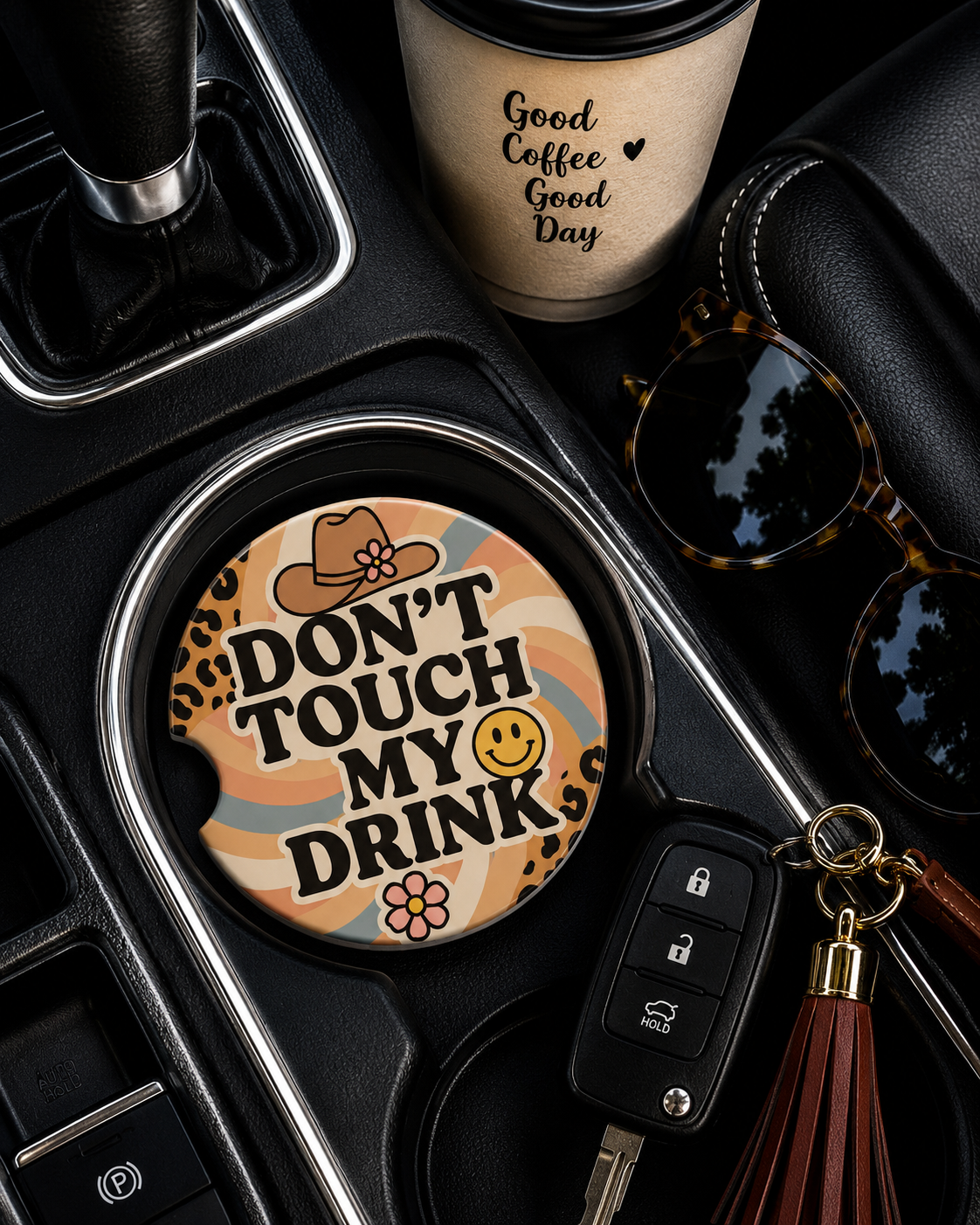 Don't Touch My Drink ceramic car coaster in cup holder — retro rainbow and leopard print design, shown in car console with coffee cup and sunglasses
