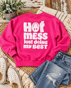 Back of the hot pink Hot Mess sweatshirt styled with distressed jeans, white sneakers, a textured throw, and greenery

