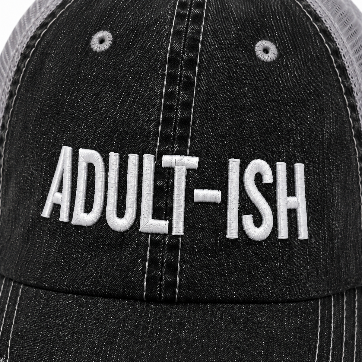 Close-up of a black distressed trucker hat with white embroidered text reading 'ADULT-ISH' on the front panel.
