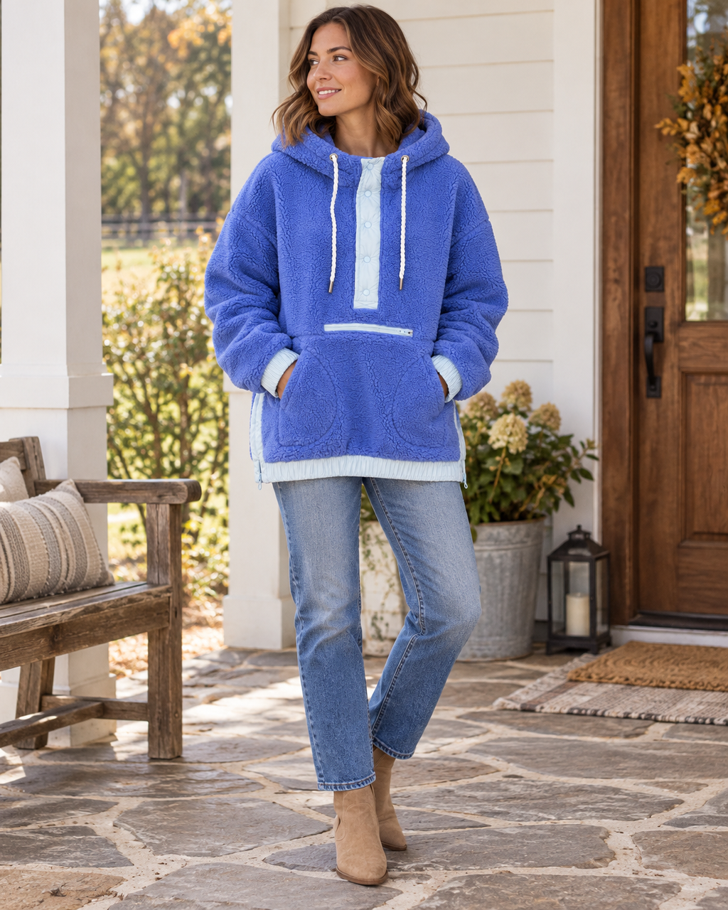 Woman wearing a blue two-toned sherpa pullover hoodie with light blue trim, rope drawstrings, and front pockets, styled with jeans and tan boots
