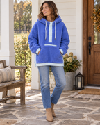 Woman wearing a blue two-toned sherpa pullover hoodie with light blue trim, rope drawstrings, and front pockets, styled with jeans and tan boots

