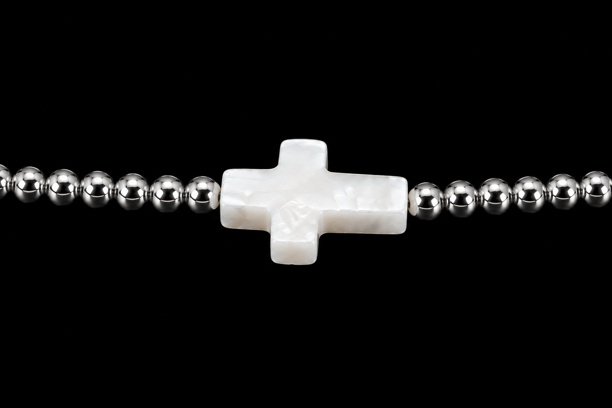 Close-up of white mother-of-pearl cross centerpiece flanked by polished silver-tone round beads on stretch bracelet
