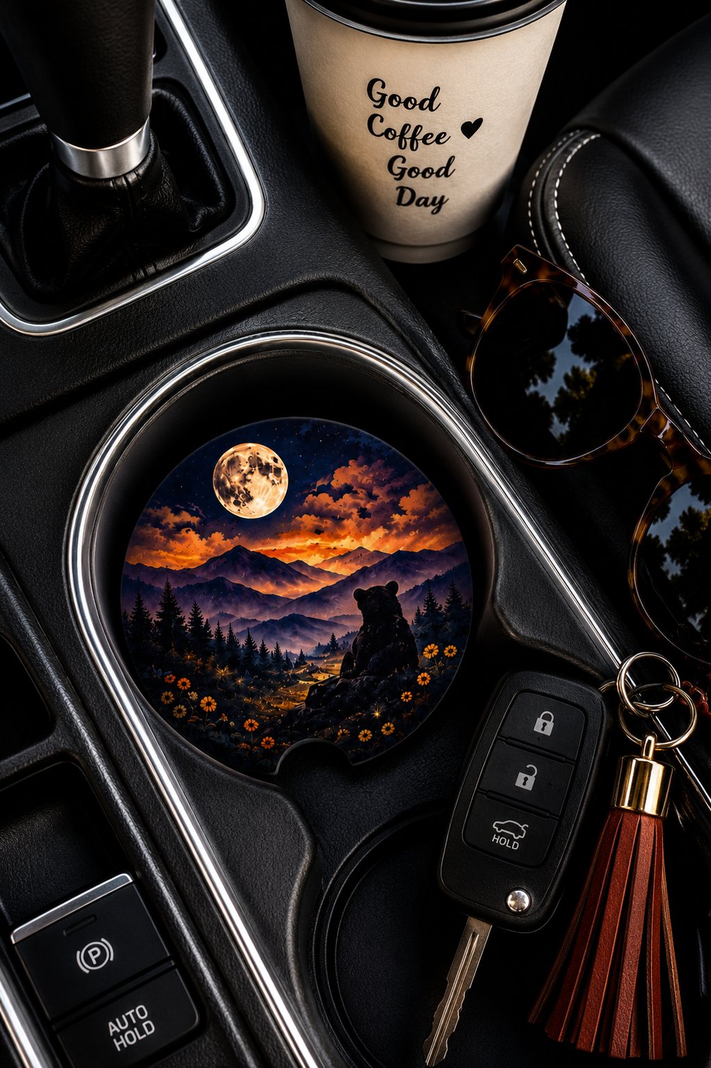 Bear Under the Full Moon ceramic car coaster in cup holder — bear and mountain night sky design, shown in car console with coffee cup and sunglasses
