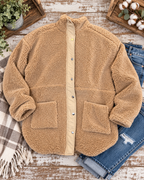 Camel sherpa teddy jacket styled with distressed jeans, a plaid fringed throw, greenery, and cotton stems on rustic wood
