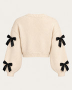 Back view of the tan cropped cardigan showing the plain knit back, black bows on the sleeves, and ribbed cuffs and hem
