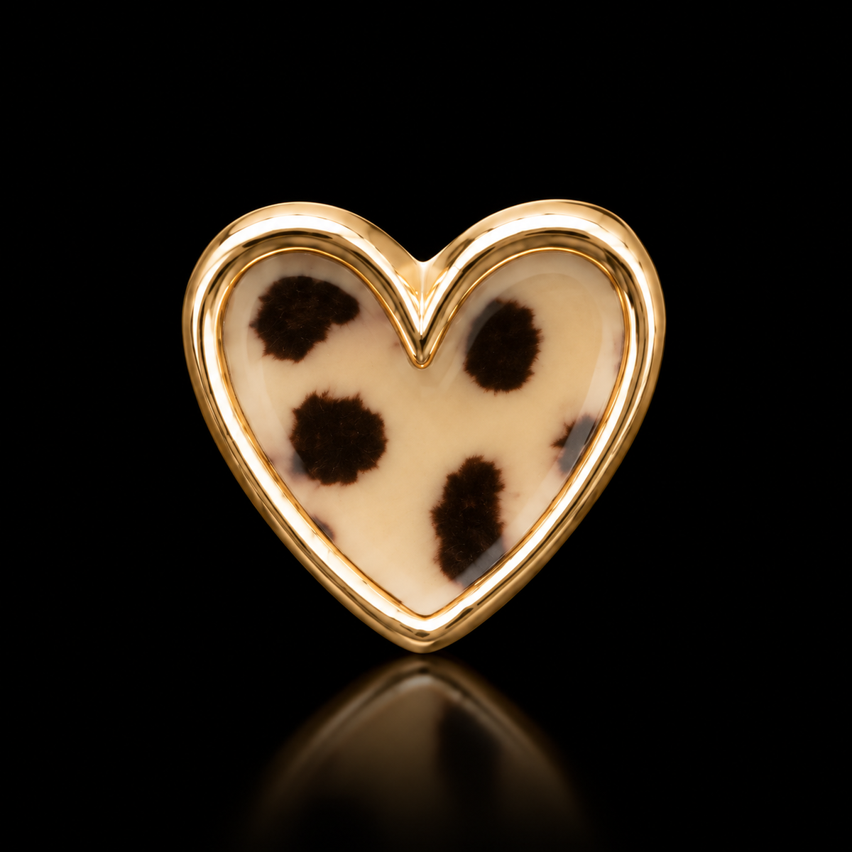 Close-up of single leopard print heart stud earring with cream and brown spots and polished gold-tone bezel setting on black reflective surface
