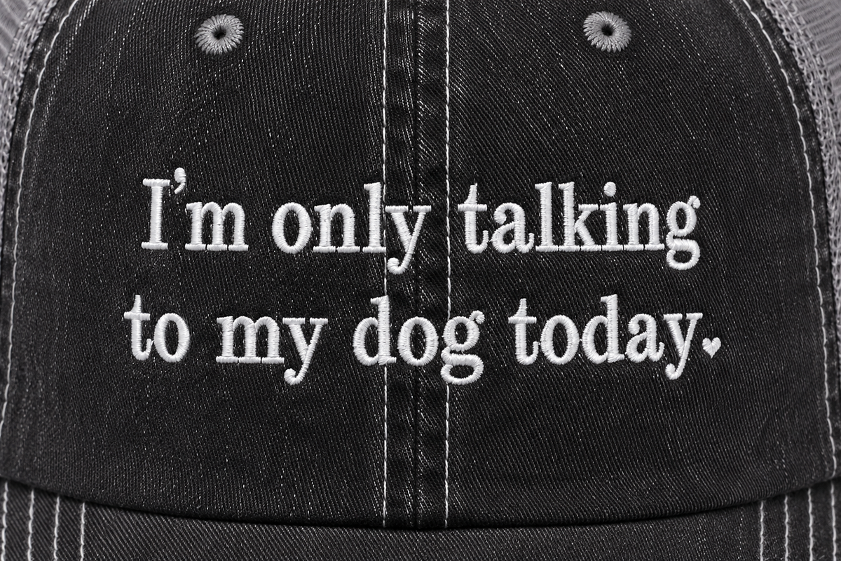 Close-up of embroidered "I'm Only Talking to My Dog Today" script on a washed black trucker hat front panel.
