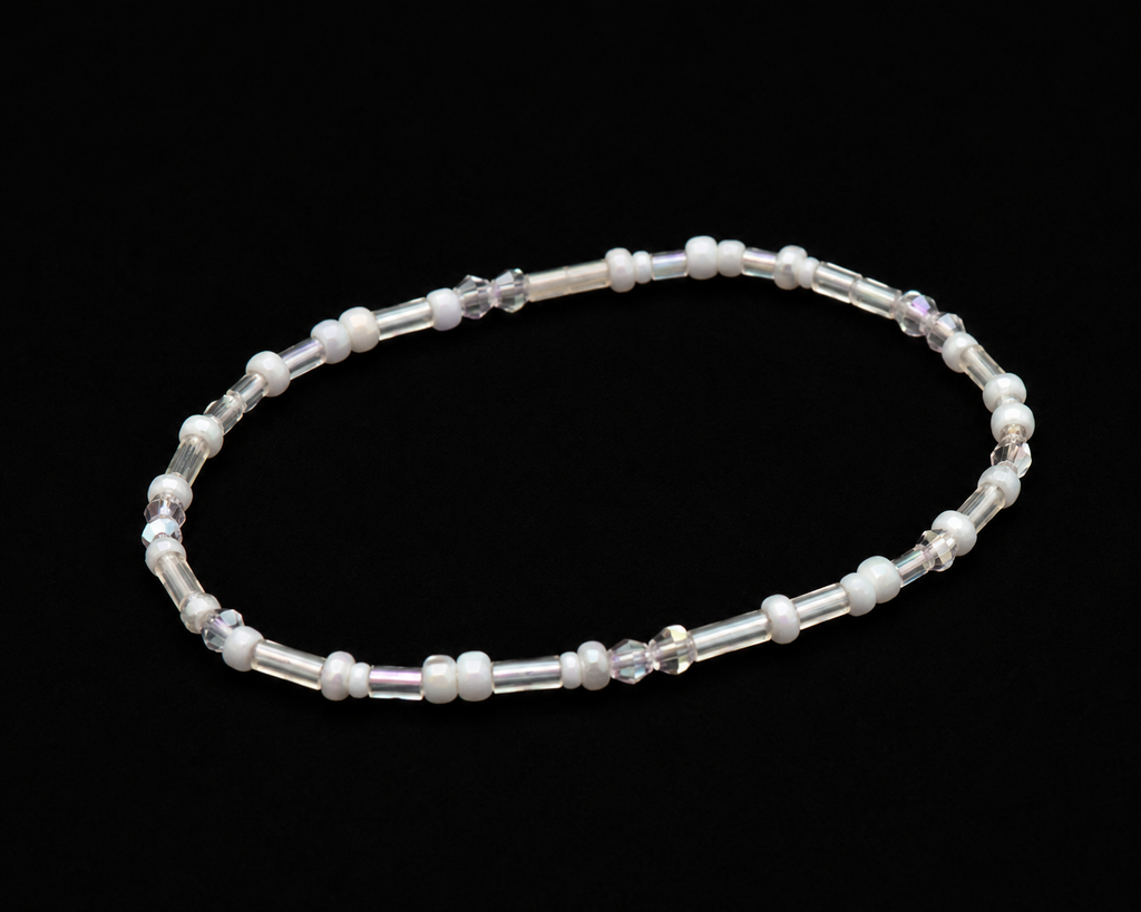 White and iridescent seed bead stretch bracelet with clear bugle beads shown at an angle on black reflective surface
