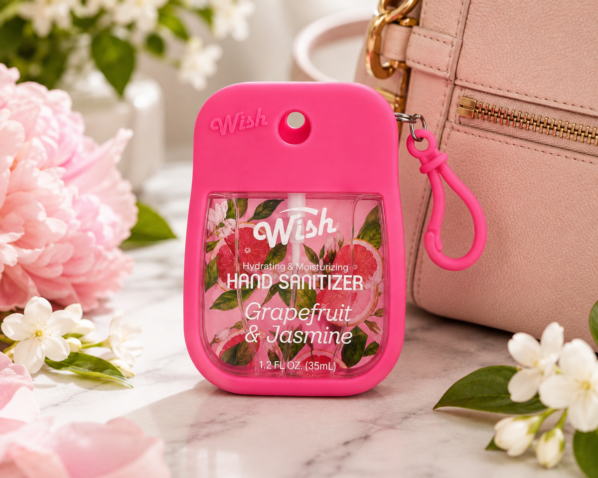 A pink Wish brand hand sanitizer bottle with a grapefruit and jasmine scent, styled on a marble surface with pink flowers and a beige handbag in the background.