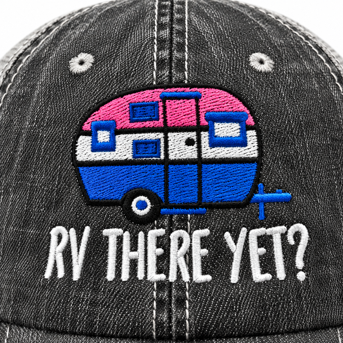 Close-up of embroidered pink and blue retro camper graphic with white RV There Yet lettering on distressed black trucker hat front panel
