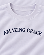 Close-up of navy Amazing Grace lettering and the ribbed crew neckline on the light lavender sweatshirt
