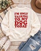 Back of the cream dog-lover sweatshirt styled with distressed jeans, white sneakers, a tan hat, and greenery on rustic wood
