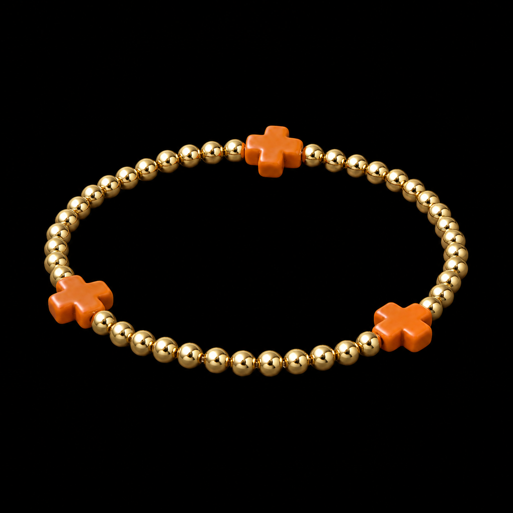 Gold ball bead stretch bracelet with orange cross accents shown at an angle on black reflective surface
