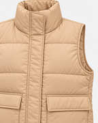 Close-up of the tan quilted puffer vest showing the tall stand collar, covered front placket, armhole trim, quilting, and pocket flap details
