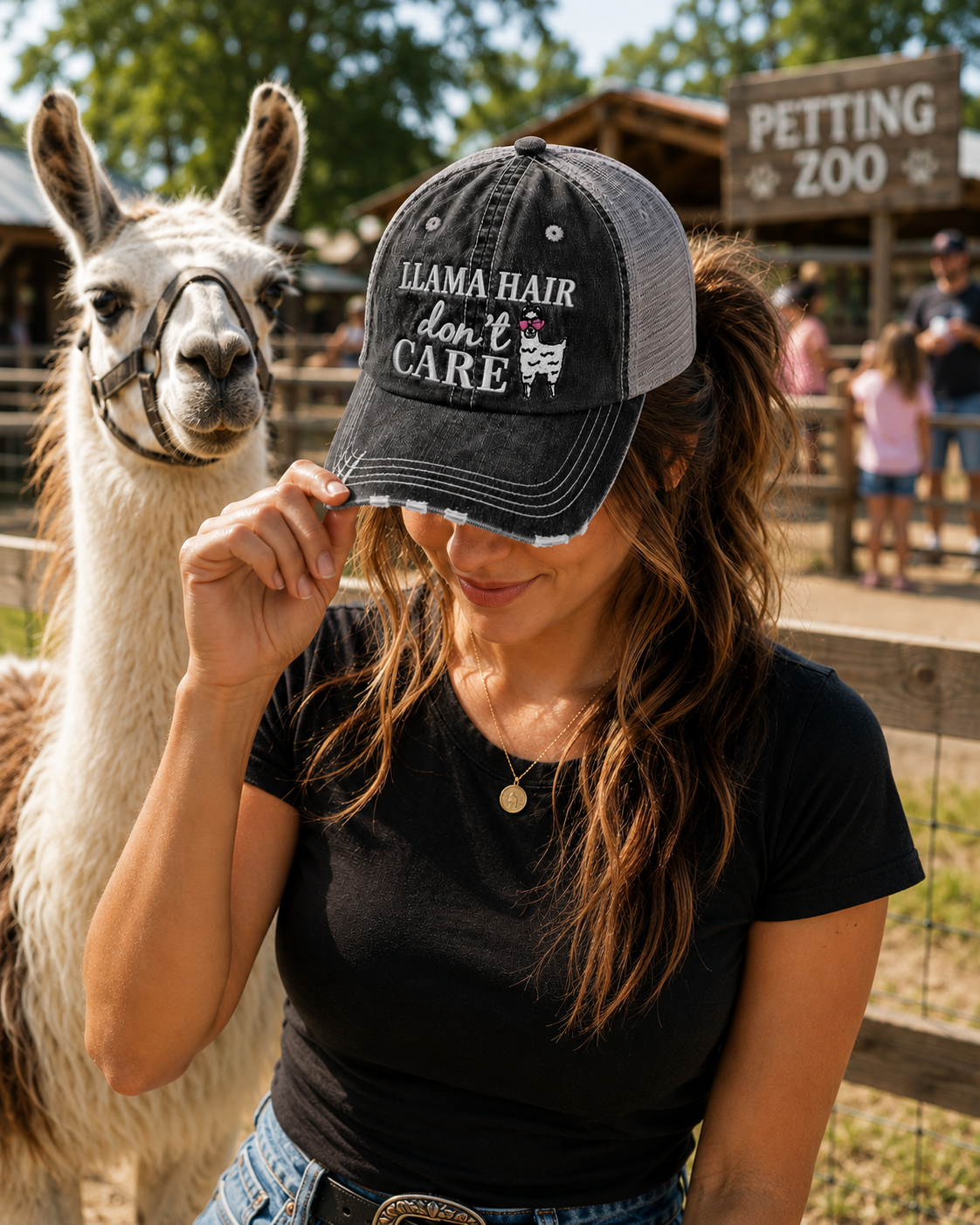 A woman at a petting zoo wearing a black and gray trucker hat with the text 'LLAMA HAIR don't CARE' and a llama graphic, posing with a llama in the background.