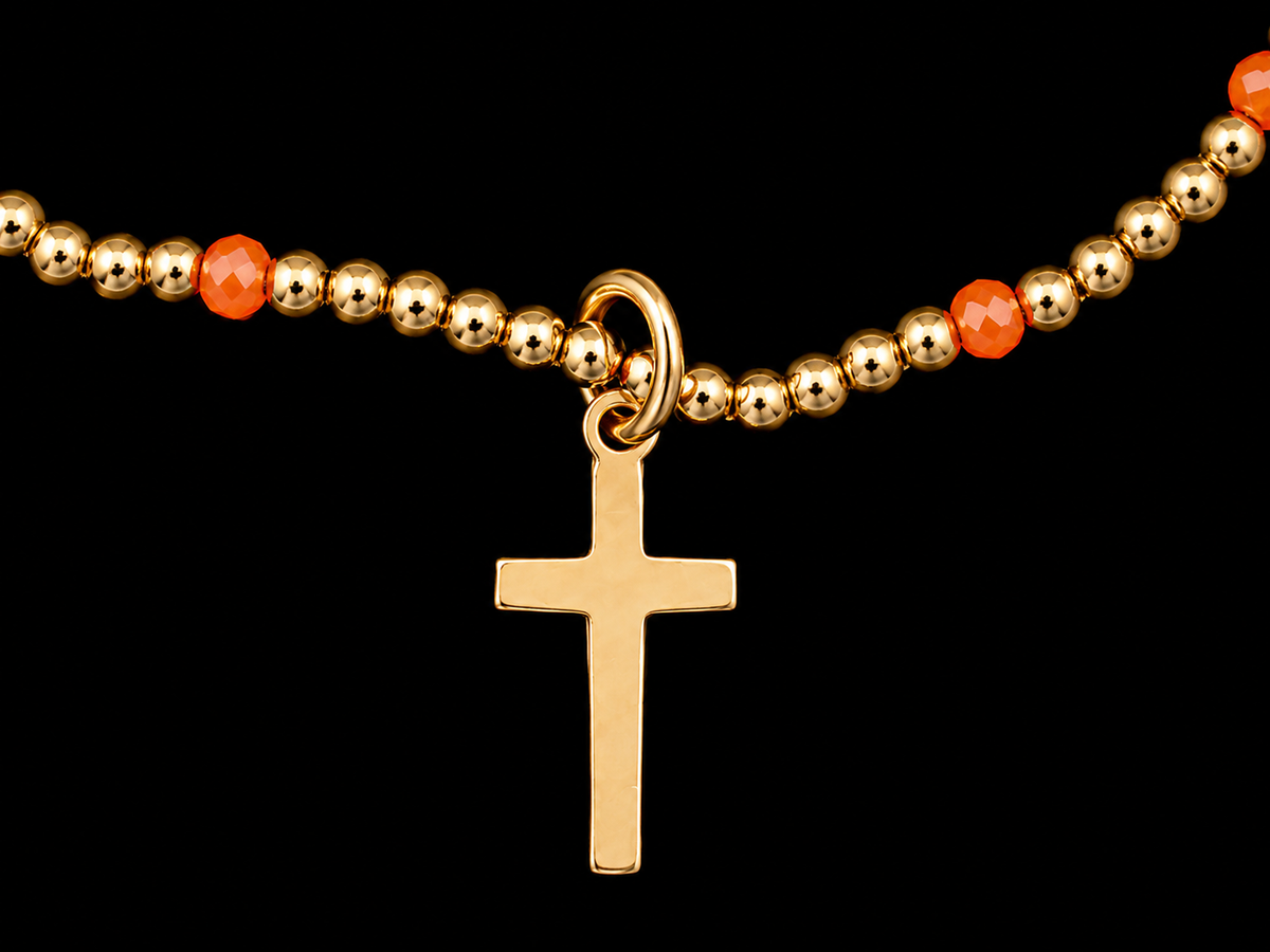 Close-up of polished gold-tone round beads, faceted orange accent beads, and gold-tone cross charm on stretch bracelet
