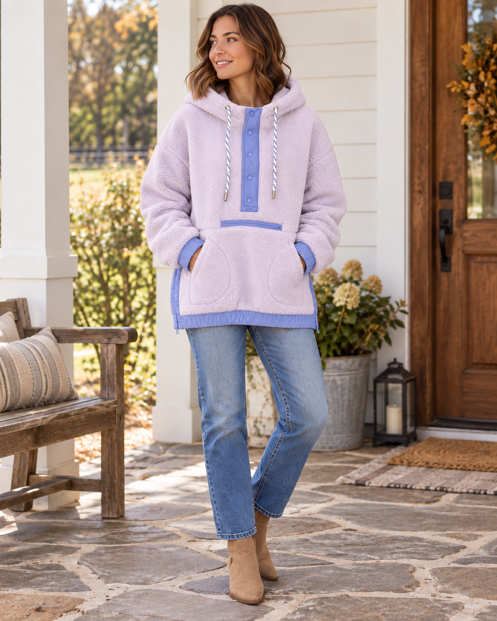 Woman wearing a light purple sherpa pullover hoodie with periwinkle blue trim and twisted drawstrings, styled with jeans and tan ankle boots
