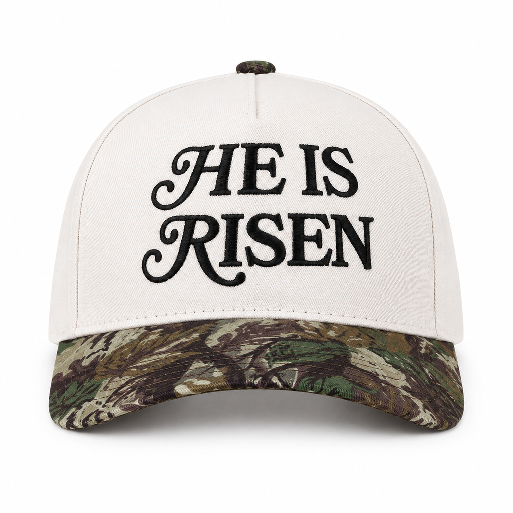 He Is Risen Baseball Cap in Camo front view showing white cotton crown with black decorative script He Is Risen embroidery, green and brown mossy oak camouflage bill, and camo top button on white background
