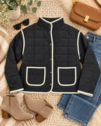 Black Quilted Contrast Trim Jacket styled in flat lay on cream sherpa and jute surface with blue jeans, tan suede block-heel ankle booties, tan structured box crossbody bag with gold clasp, black round sunglasses, and eucalyptus and baby's breath florals

