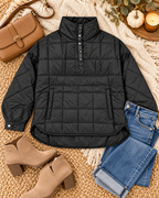 Black Quilted Puffer Pullover Jacket styled in flat lay on cream chunky knit throw on jute rug with folded blue jeans, tan suede block-heel ankle booties, tan leather saddle crossbody bag, mini white pumpkin, amber glass candle on wood disc, and eucalyptus sprigs
