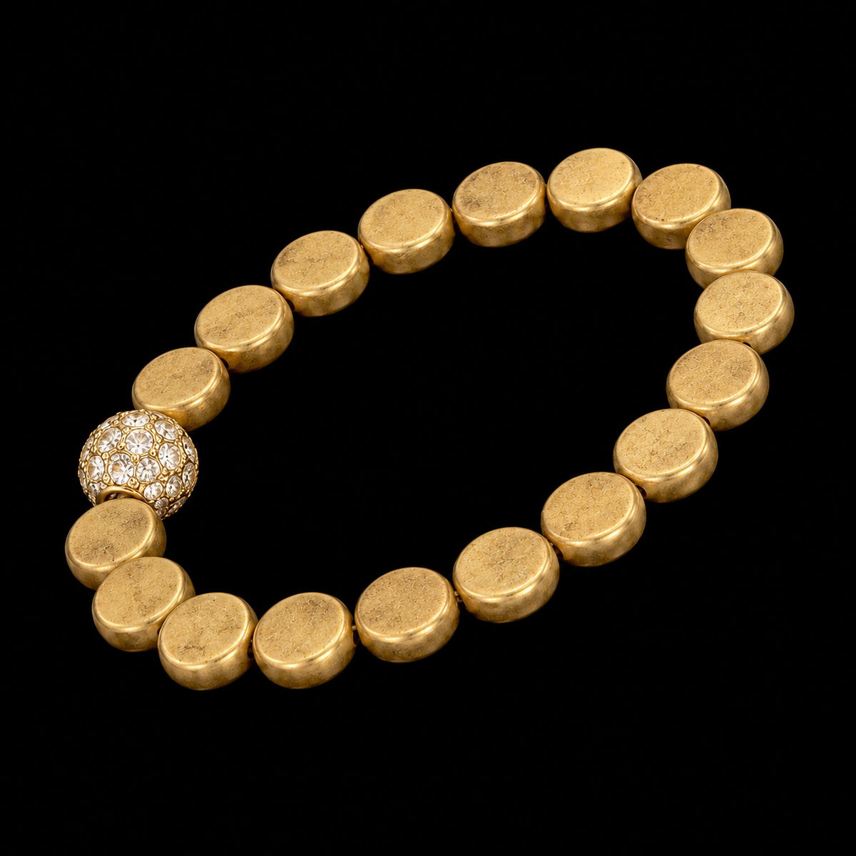 Gold coin bead stretch bracelet with crystal accent bead shown at an angle on black reflective surface
