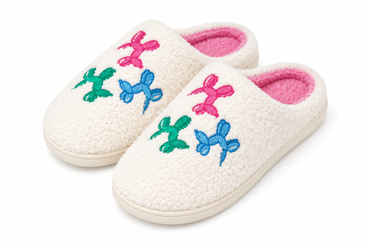 Pair of Ivory Balloon Dog Fuzzy Slippers at an angle showing pink, blue, and green embroidered balloon dogs on ivory fuzzy exterior with bright pink plush interior and cream rubber sole
