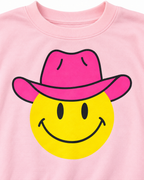 Close-up of the yellow smiley face with black eyes and smile wearing a hot pink cowboy hat on light pink fabric
