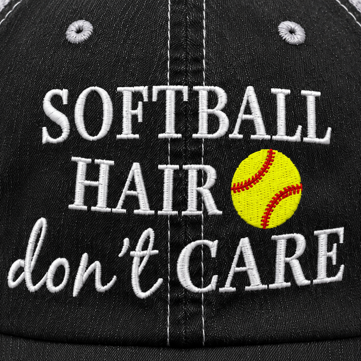 Softball Hair Don’t Care trucker hat close-up showing white embroidered lettering and bright yellow softball design on distressed black fabric.