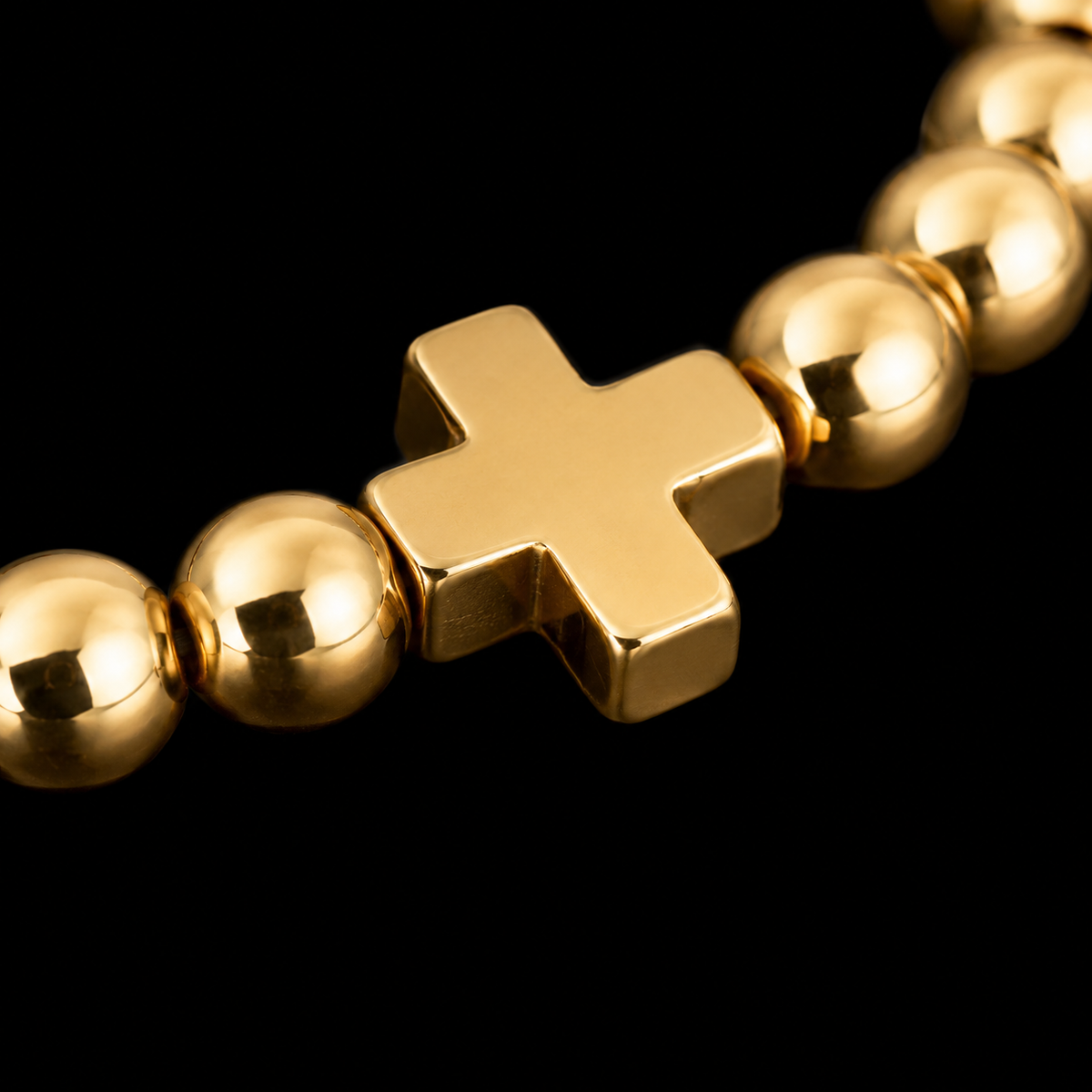 Close-up of polished gold-tone cross bead accent flanked by round gold beads on stretch bracelet
