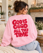 Model showing the red God Is Good All the Time back graphic on a pink sweatshirt, paired with jeans
